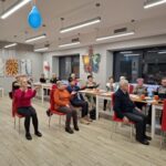 grupa osób siedzi na krzesłach i wykonuje ćwiczenia gimnastyczne