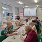 grupa osób siedzi przy stołach i rozwiązują zadania