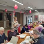 grupa osób siedzi przy stołach i rozwiązują zadania pisemne