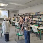 grupa osób wykonuje gimnastykę przy krzesłach