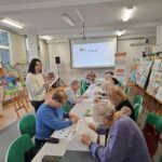 grupa osób siedzi przy stołach i rozwiązują zadania