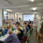 grupa osób siedzi przy stołach i rozwiązują zadania