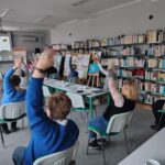 grupa osób siedzi i wykonuje gimnastykę na krzesłach