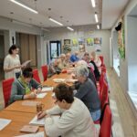grupa seniorów siedzi przy stołach i rozwiązuje zadania na pamięć i koncentrację