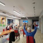 grupa seniorów wykonuje gimnastykę na krzesełkach