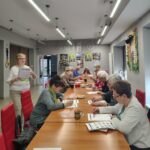 grupa seniorów siedzi przy stołach i rozwiązuje zadania na pamięć i koncentrację