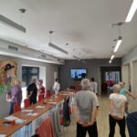 grupa seniorów wykonuje gimnastykę na stojąco