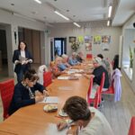 grupa seniorów siedzi przy stołach i rozwiazuja zadania