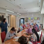 grupa seniorów siedzi przy stołach i rozwiązują ćwiczenia na pamięć i koncentrację