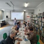 grupa seniorów siedzi przy stołach rozwiązując zadania