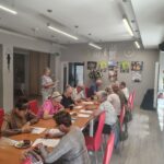 grupa seniorów siedzi przy stołach i rozwiązują zadania