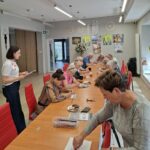 grupa seniorów siedzi przy stołach i rozwiązują zadania