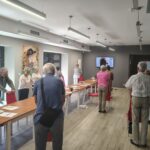 grupa seniorów stoi przy krzesłach i się gimnastykuje