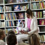 bibliotekarka trzyma jednorożca, który opowiada dzieciom bajki