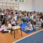 dzieci siedzą na materacach i ławkach