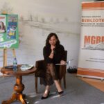 kobieta siedzi na fotelu, trzyma mikrofon, opowiada o książce