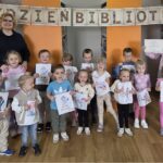 grupowe zdjęcie dzieci, ich Pani oraz bibliotekarki, w tle napis Tydzień Bibliotek